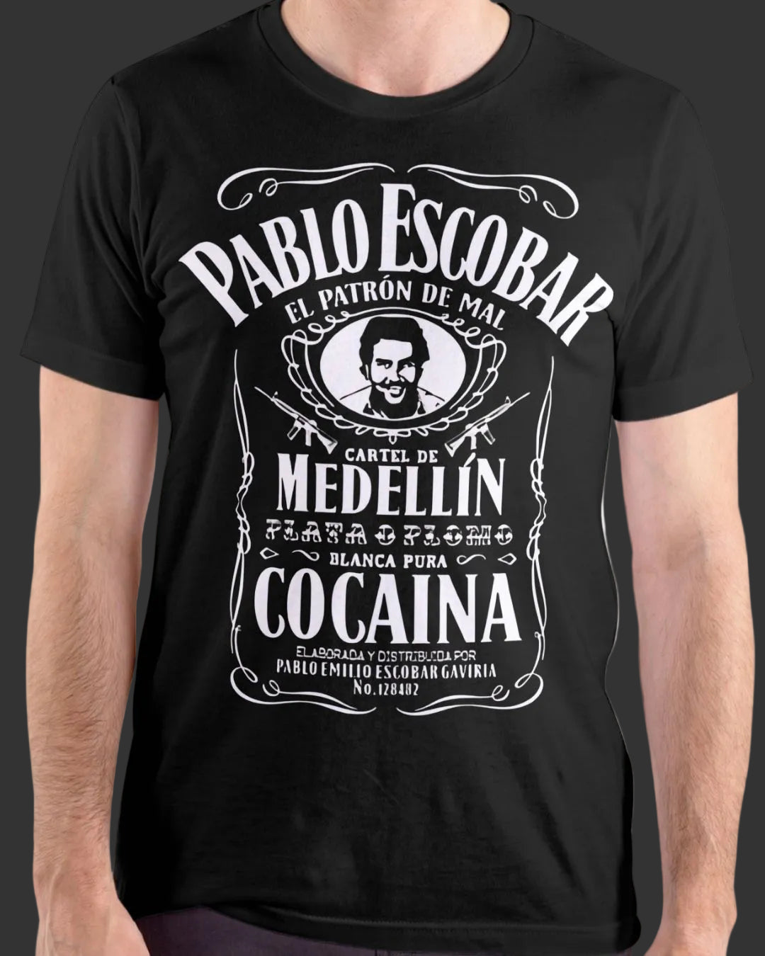 A man wearing a black short-sleeve t-shirt with a large white graphic print styled like a vintage Pablo Escobar Medellin Cocaina label.